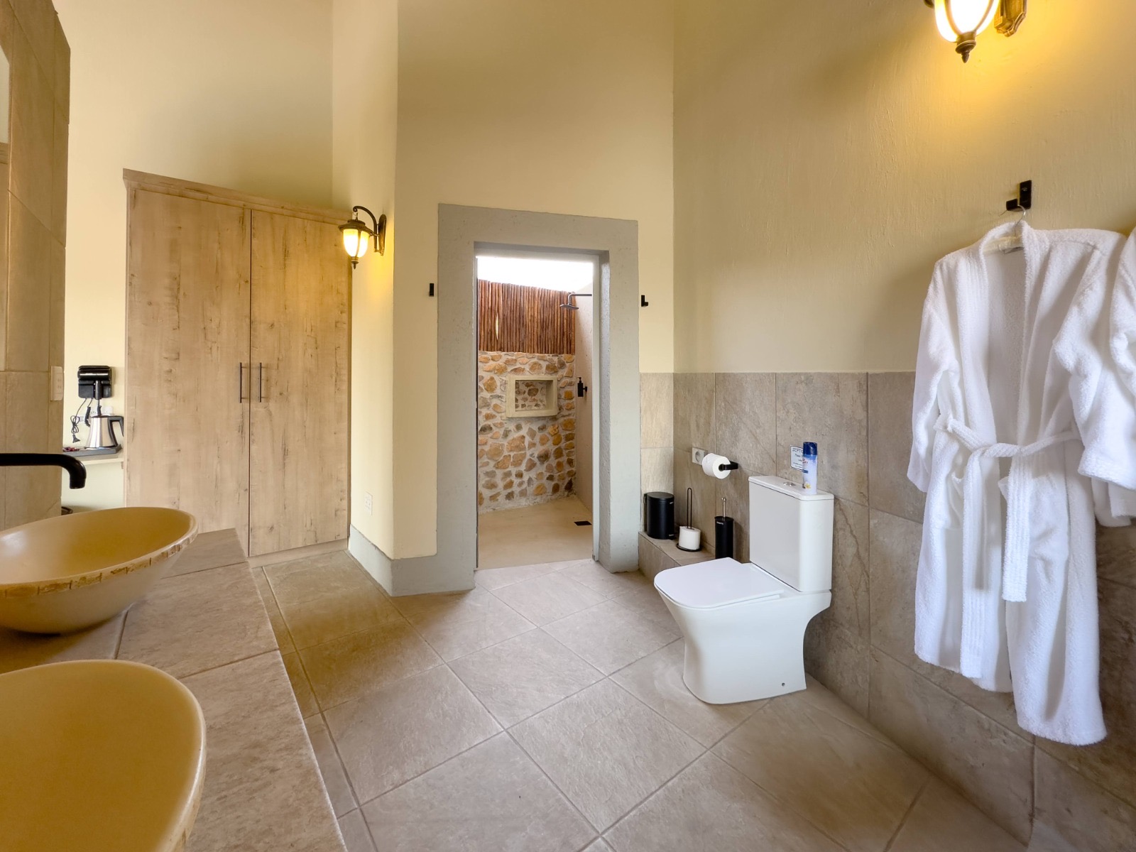 En-suite bathroom with twin stone basins, robes and a doorway to the open-air stone shower at Tebuah