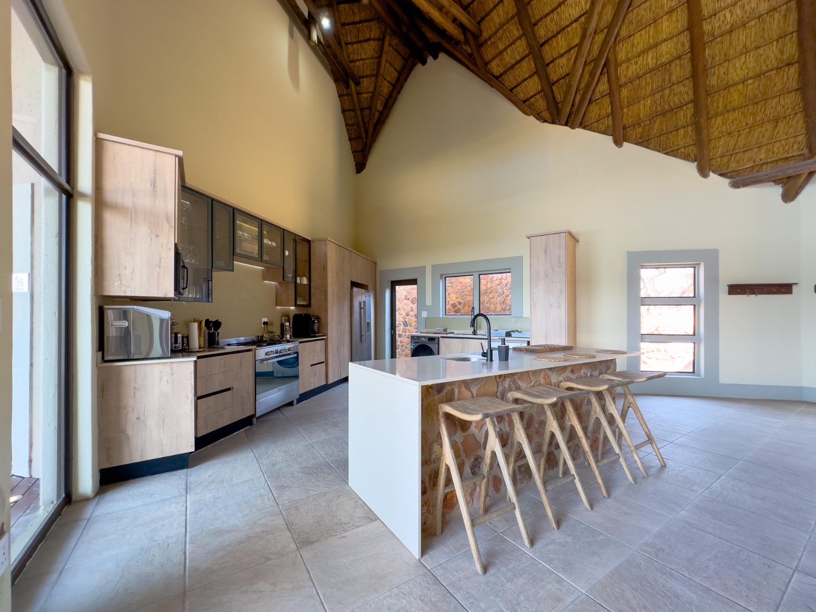 Open self-catering kitchen with stone island, bar stools and high thatched roof at Tebuah Private Lodge