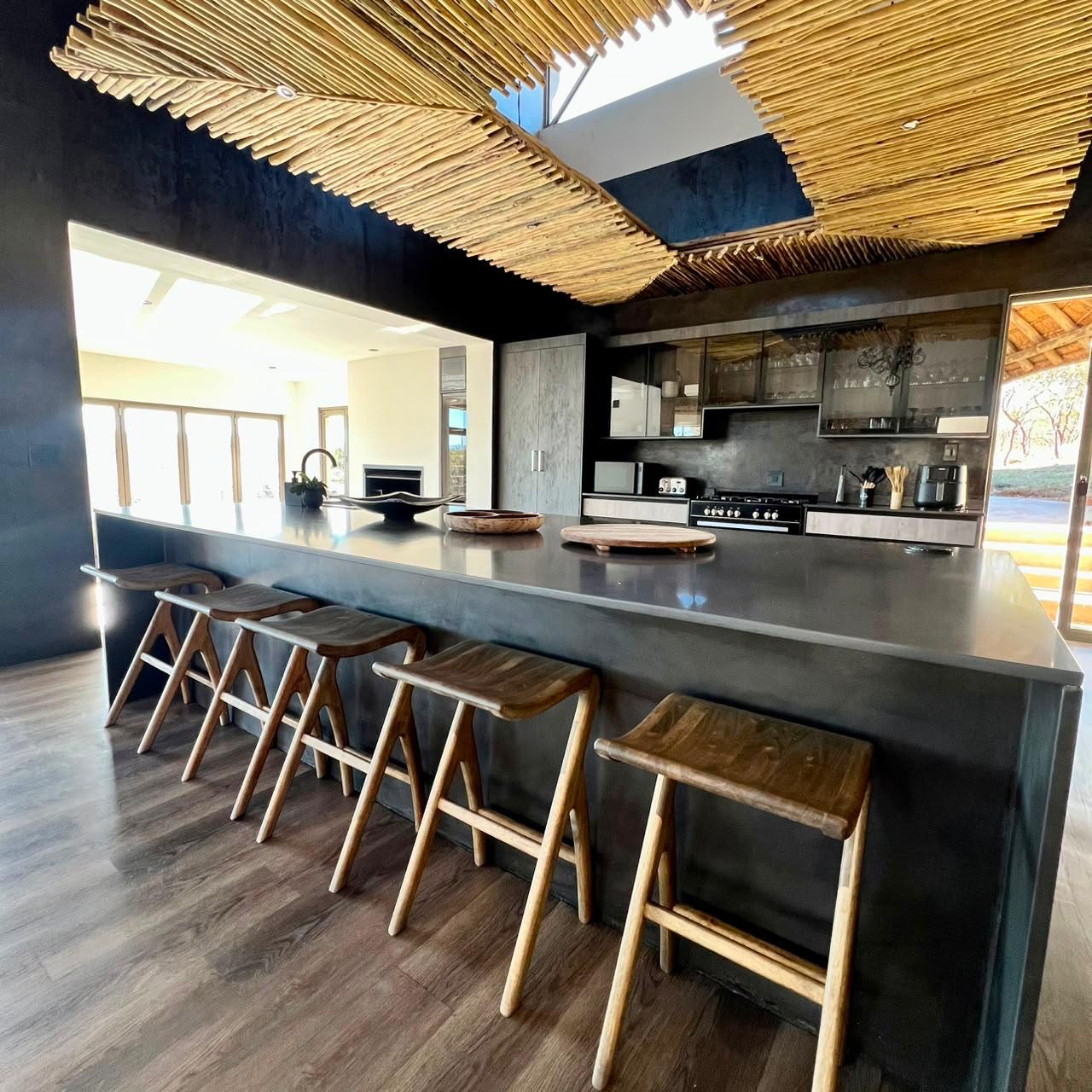 Open-plan kitchen island with bar stools under a woven reed ceiling at Sithrah Private Lodge