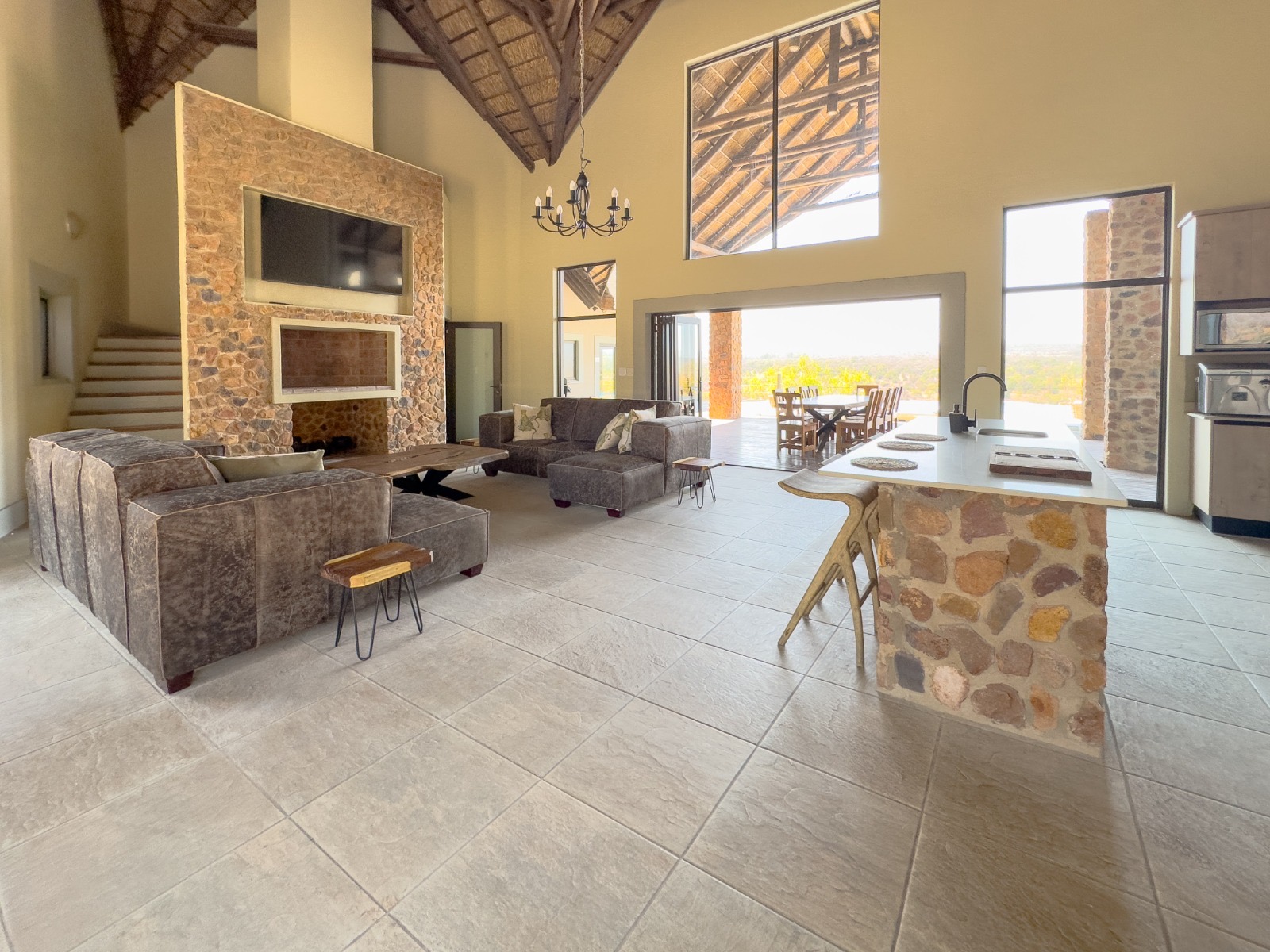 Double-volume lounge with stone fireplace, dining table and open kitchen inside Tebuah Private Lodge