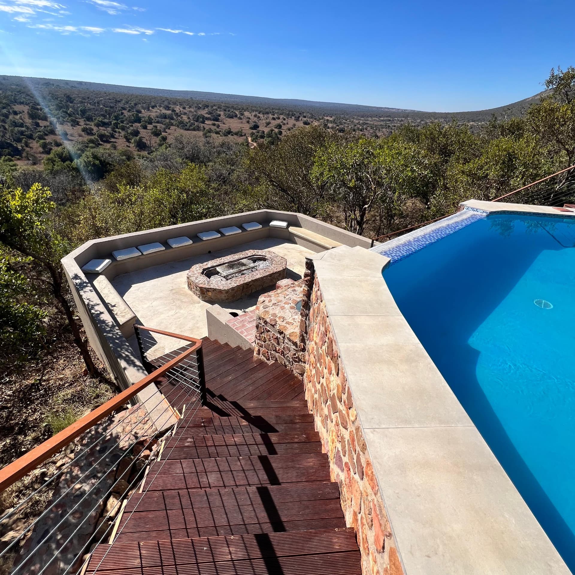 Stone firepit and curved boma seating below the pool deck at Tebuah Private Lodge